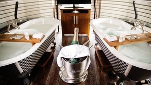 Dos jacuzzis separados con champán en el centro, una bandeja de madera y un televisor al fondo.