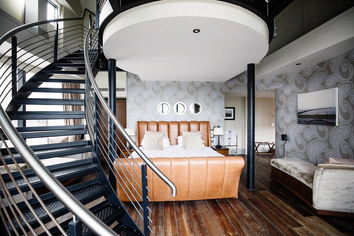 A bedroom with a curved staircase, a large bed, and a modern ceiling light fixture.
