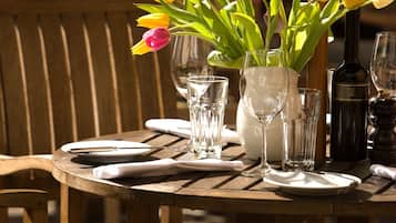 A wooden table set for dining with a vase of tulips, wine glasses, and a bottle.