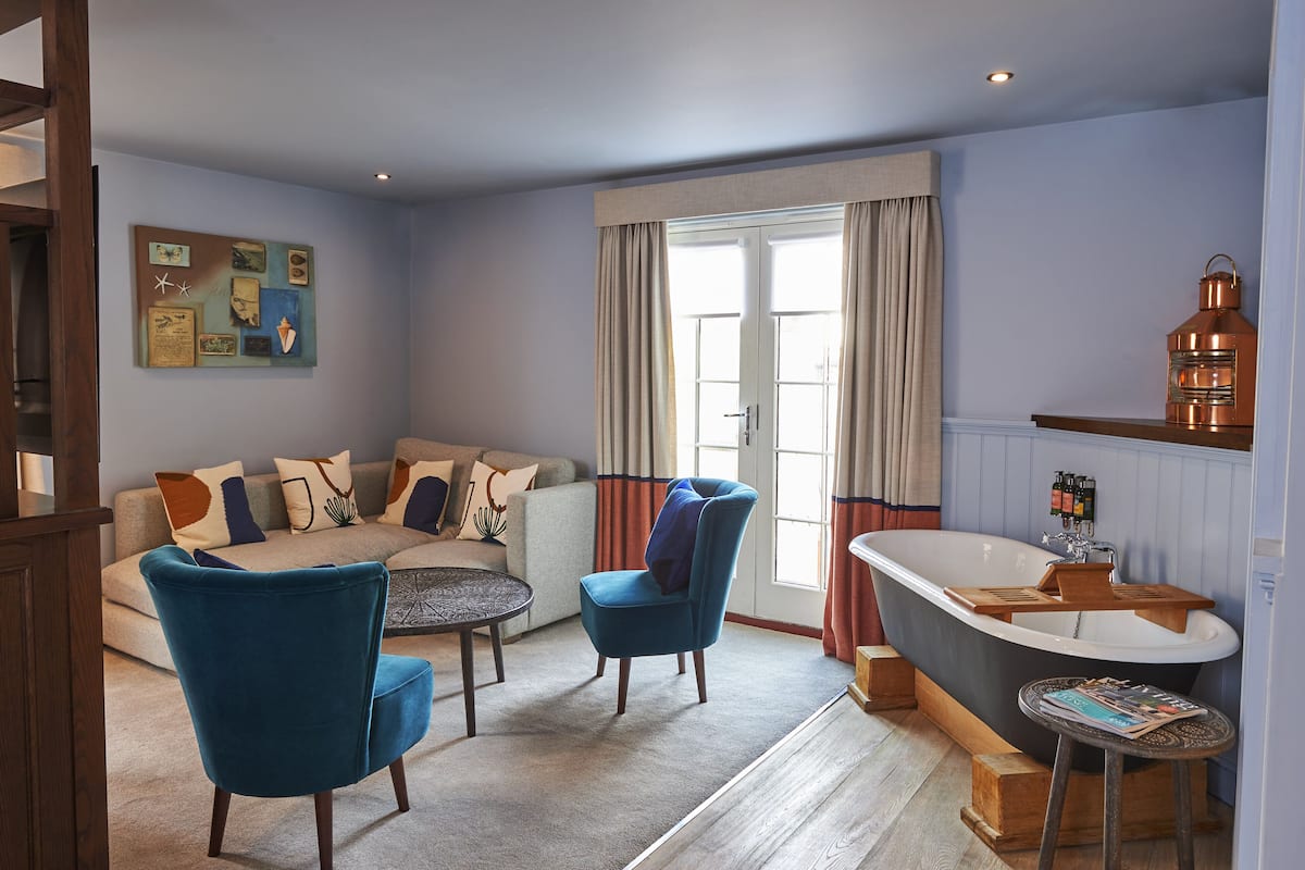 Una sala de estar con un sofá, dos sillones, una mesa de centro y una bañera con estante de madera.