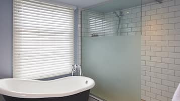 A bathroom with a freestanding bathtub, a glass shower enclosure, and a window with blinds.