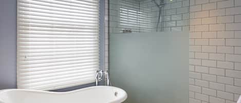 A bathroom with a freestanding bathtub, a glass shower enclosure, and a window with blinds.
