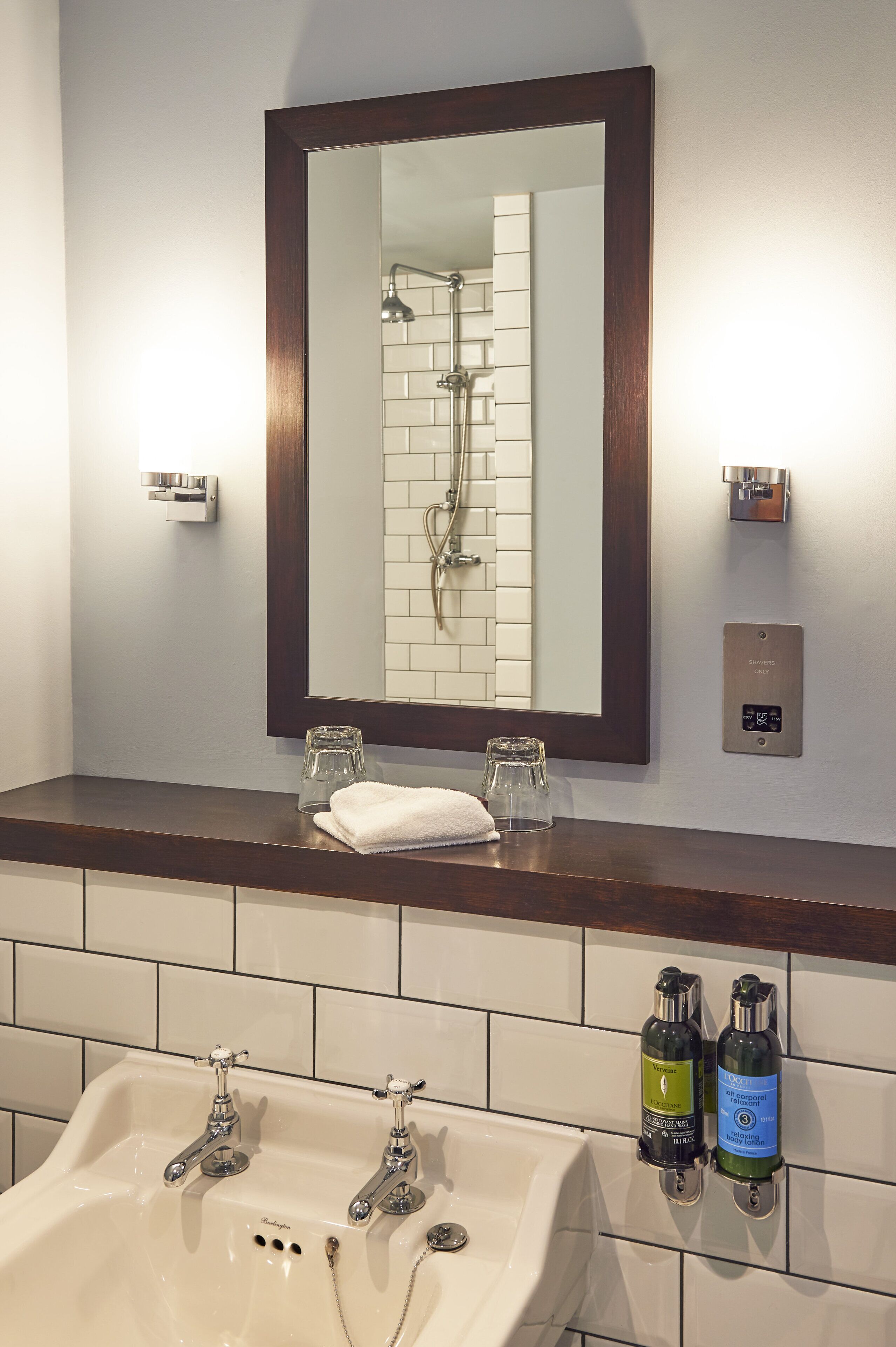 Un baño con un espejo grande, un lavabo con dos grifos y dos botellas de champú y acondicionador en la pared.