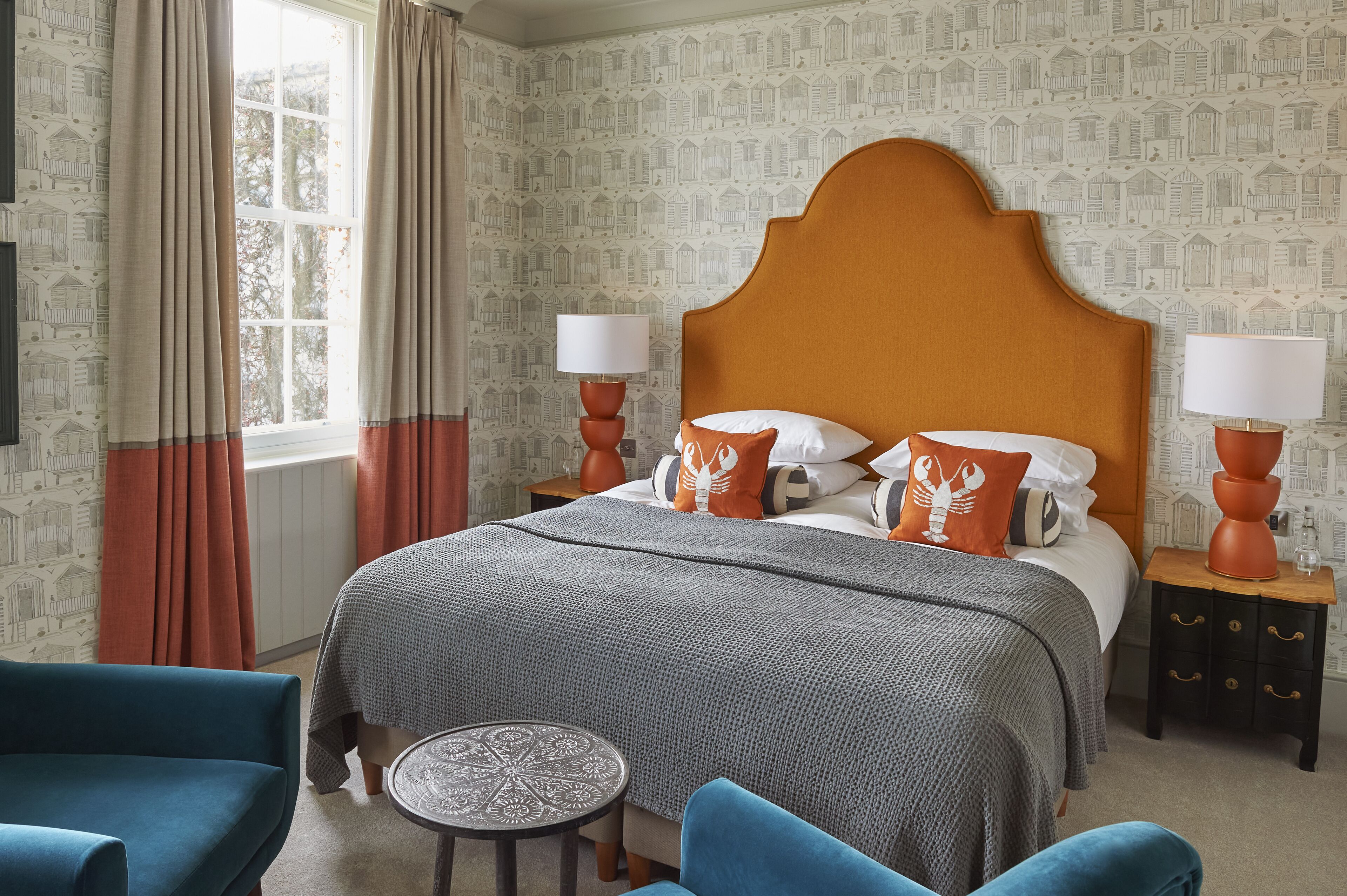 A neatly arranged bedroom with a large bed, two bedside tables, a small round table, and two blue armchairs.
