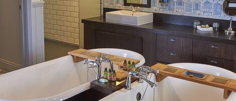 A bathroom with two freestanding tubs, a wooden vanity, and a patterned wall.