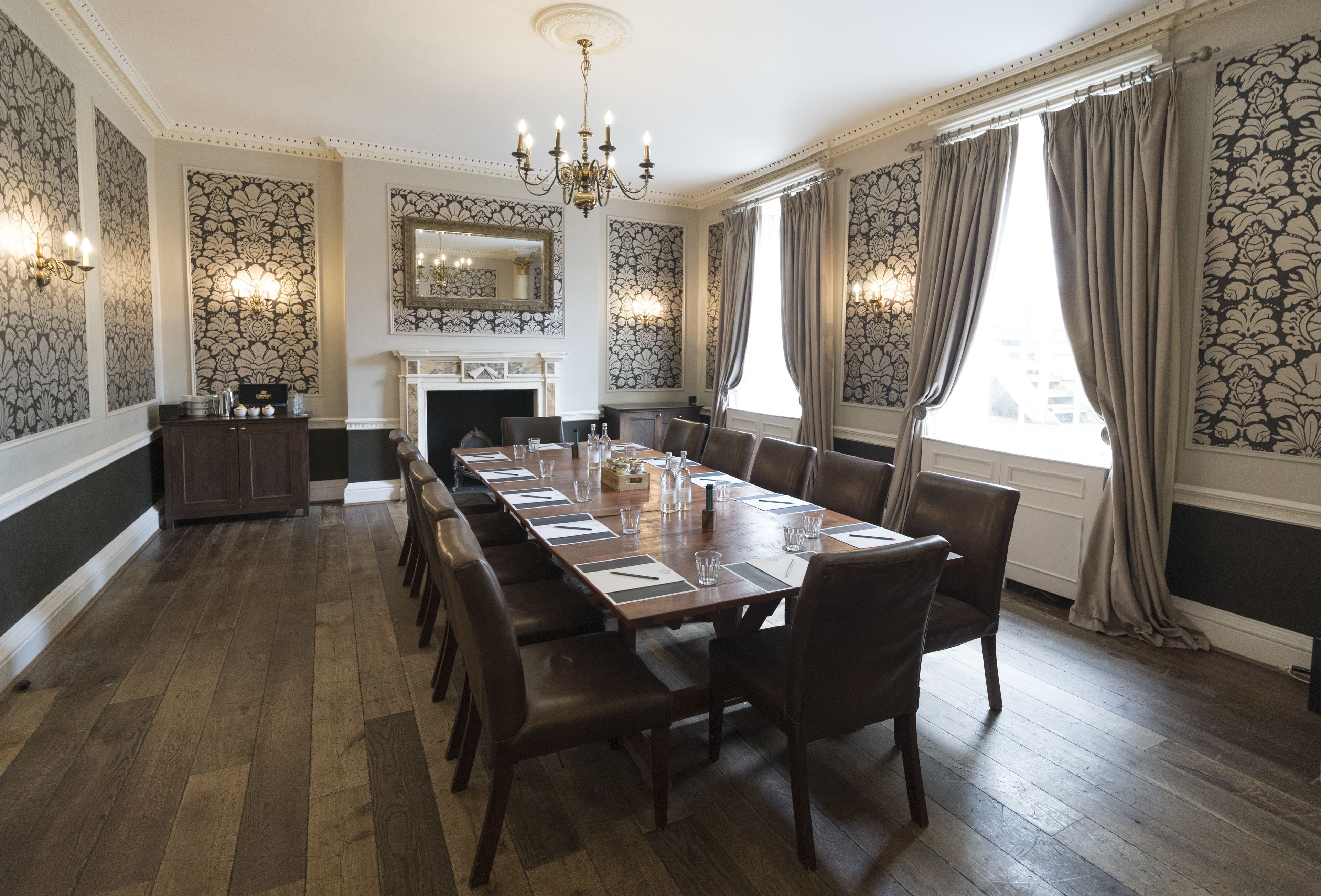 A formal dining room with a long table, chairs, a chandelier, and patterned wallpaper.