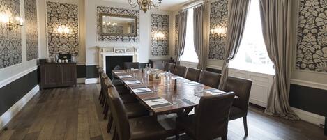 A formal dining room with a long table, chairs, a chandelier, and patterned wallpaper.