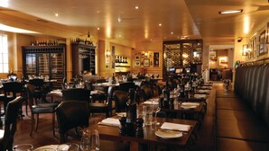 A restaurant with multiple tables and chairs, a bar area with bottles, and a seating area with a high ceiling and warm lighting. - Hotel du Vin & Bistro Poole (Poole)