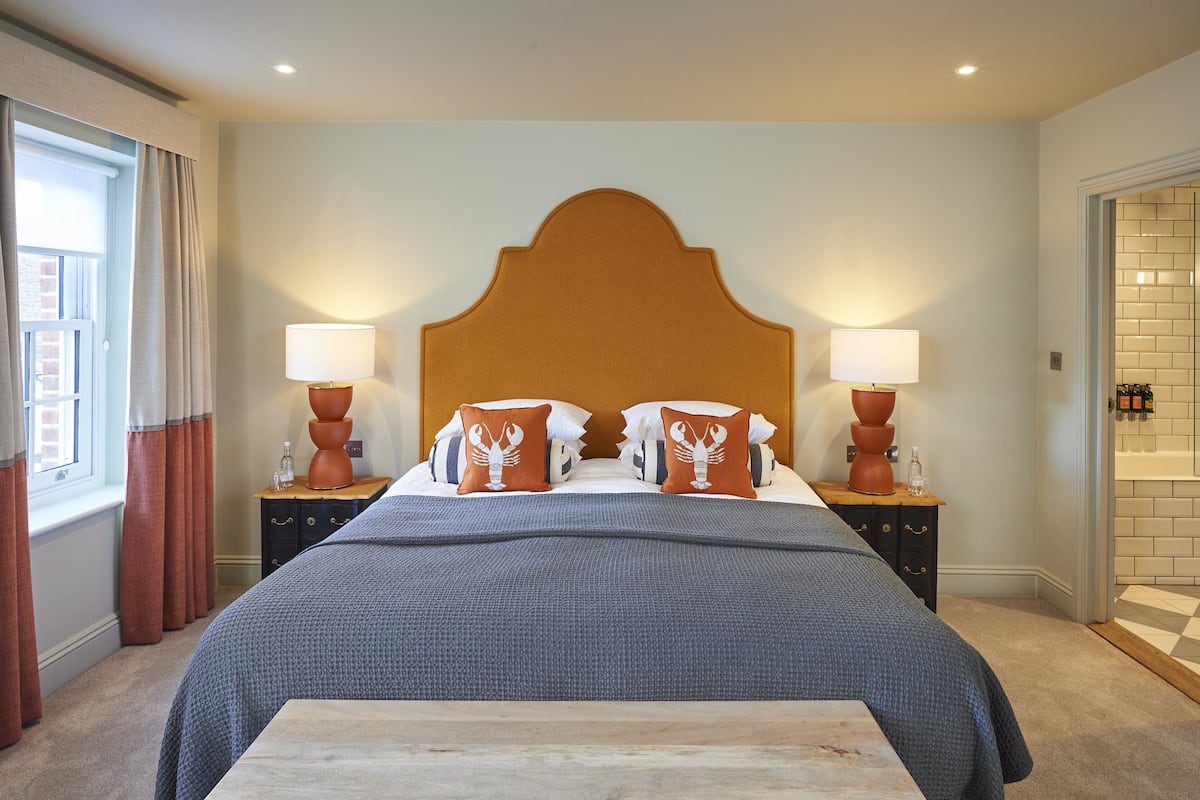 Una cama bien hecha con cabecera de madera, dos lámparas de noche y una ventana con cortinas.