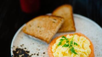 A plate with scrambled eggs and a slice of salmon, accompanied by two pieces of toast on a speckled ceramic plate.