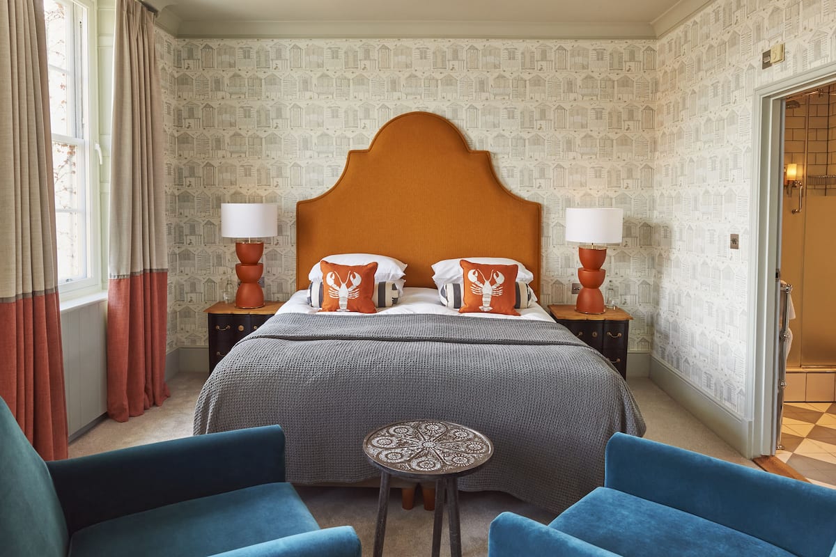 Habitación de hotel con una cama grande, dos mesitas de noche, una mesita pequeña y dos sillones azules.