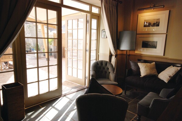 A living room with a dark leather sofa, a tufted armchair, and a small coffee table. A large window with curtains allows natural light to enter. - Hotel du Vin & Bistro Poole (Poole)