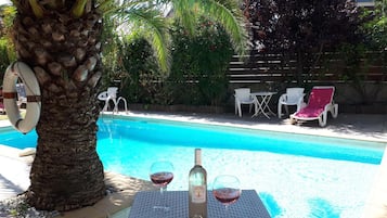 Relax by the serene pool surrounded by lush tropical plants and a palm tree, perfect for unwinding and socializing.