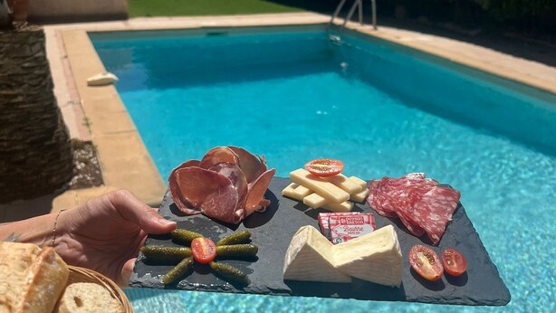 A poolside view with a black slate board displaying various cheeses, cured meats, and pickles. - Adonis Arc Hôtel Aix (Aix-en-Provence)