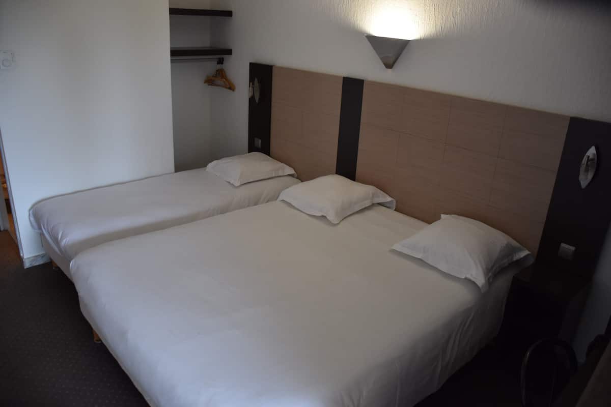 Une chambre d’hôtel avec deux lits simples, une armoire et un luminaire fixé au mur.