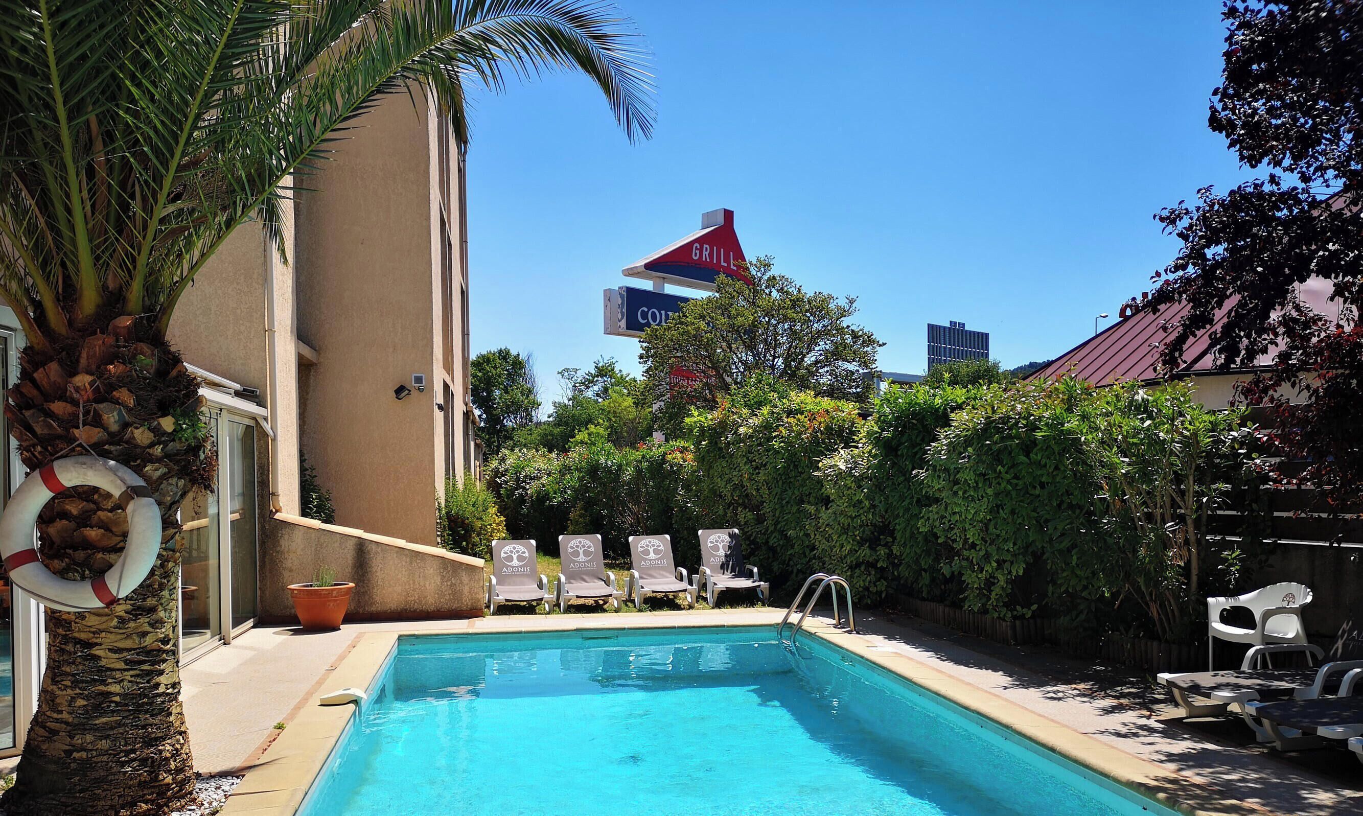 A swimming pool with lounge chairs, a palm tree, and a building with a 'GRILL' sign.