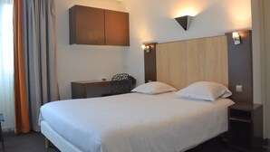 A hotel room with a large bed, a desk, a chair, and a wardrobe. - Adonis Arc Hôtel Aix (Aix-en-Provence)