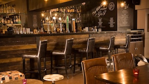 A bar area with multiple stools and a table, a bar counter with various bottles, and a menu on the wall.