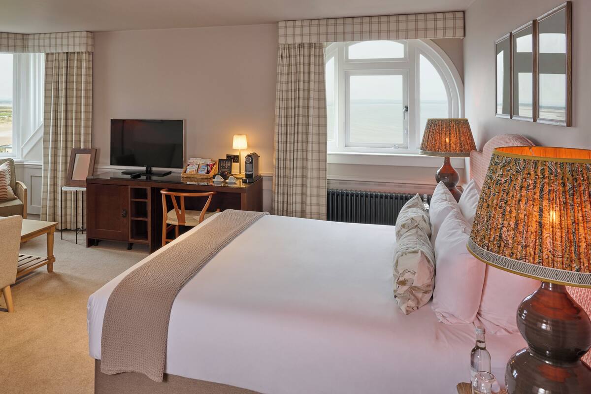 Ein Hotelzimmer mit Bett, Schreibtisch, Fernseher und Blick auf den Strand.