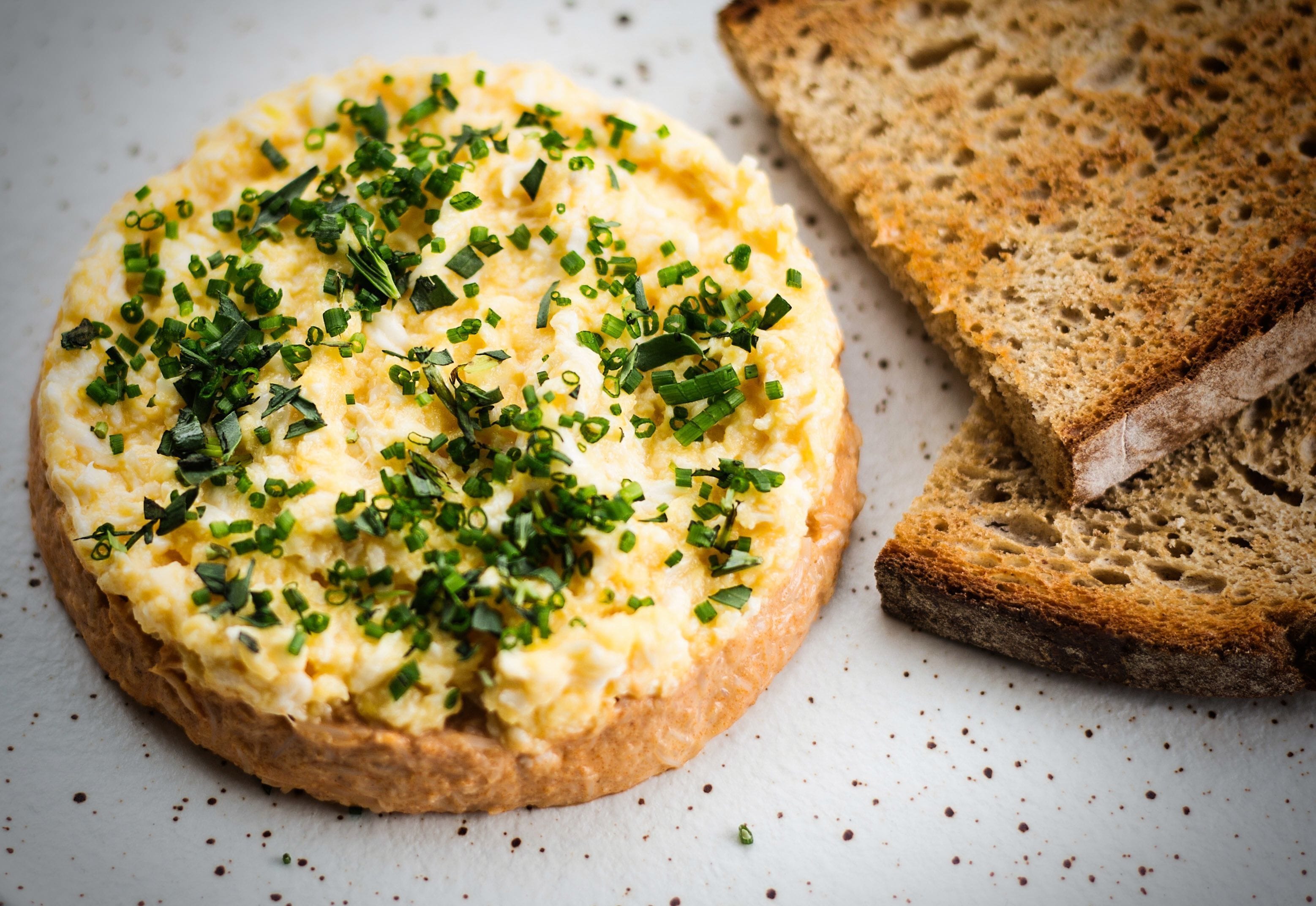 A round dish of scrambled eggs topped with chopped green onions, accompanied by slices of whole grain bread.
