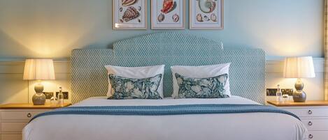 A neatly made bed with floral pillows, a patterned headboard, and framed artwork above.