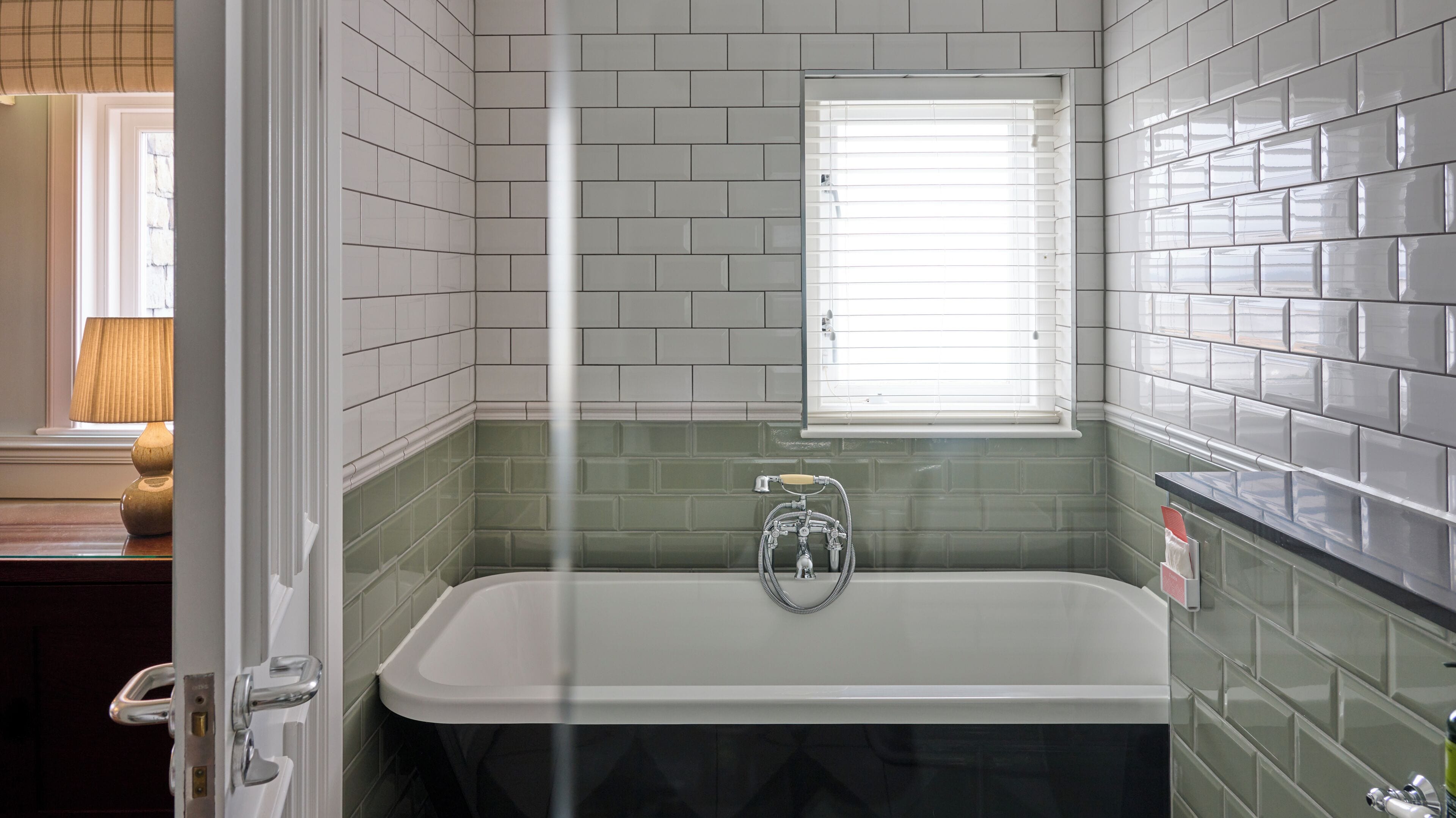 A bathroom with a bathtub, a window, and green tiled walls.