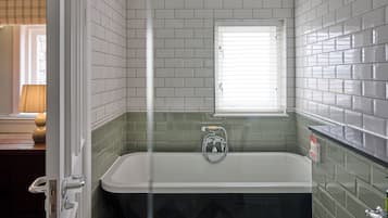 Un baño con bañera, ventana y paredes de azulejos verdes.