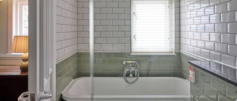 Un baño con bañera, ventana y paredes de azulejos verdes.
