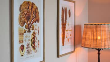Two framed botanical illustrations on a wall, a lamp with a plaid shade, and a wall-mounted light fixture.
