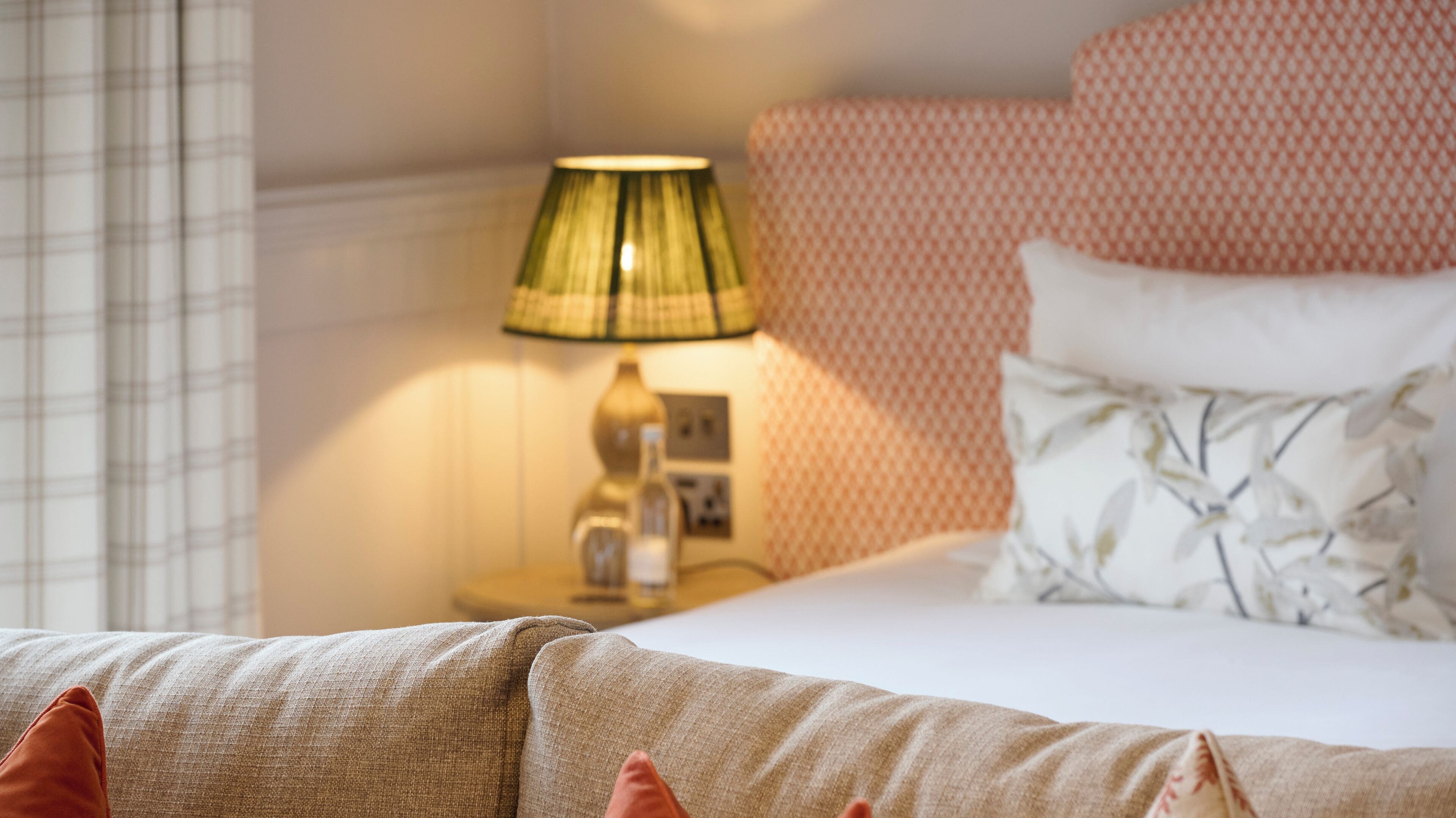 A neatly made bed with a patterned headboard, a bedside lamp, and a floral pillow.