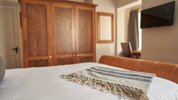 A bedroom with a large bed, a wooden wardrobe, a television mounted on the wall, and a brown leather chair.