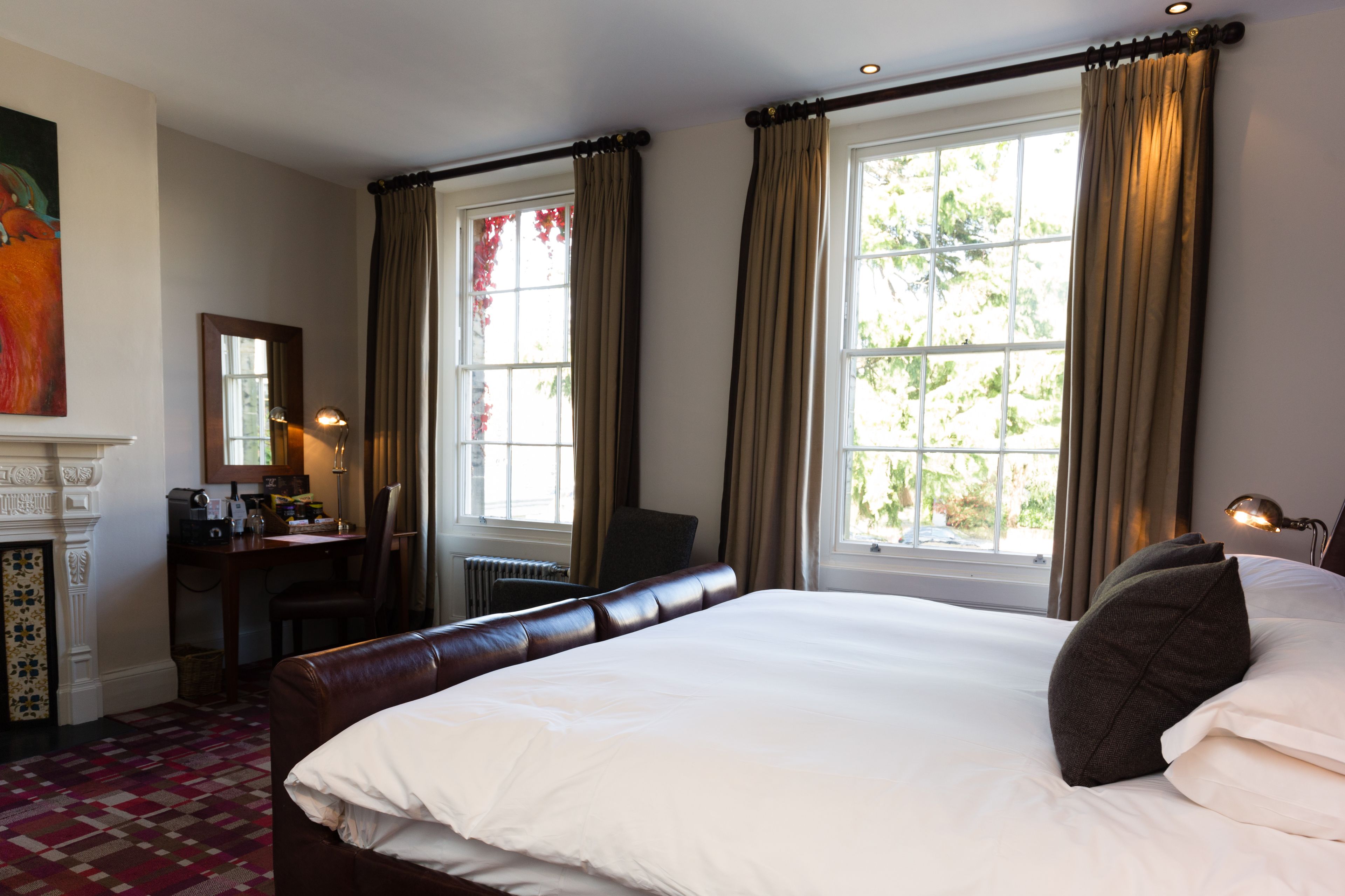A hotel room with a large bed, a desk, a chair, and a fireplace.