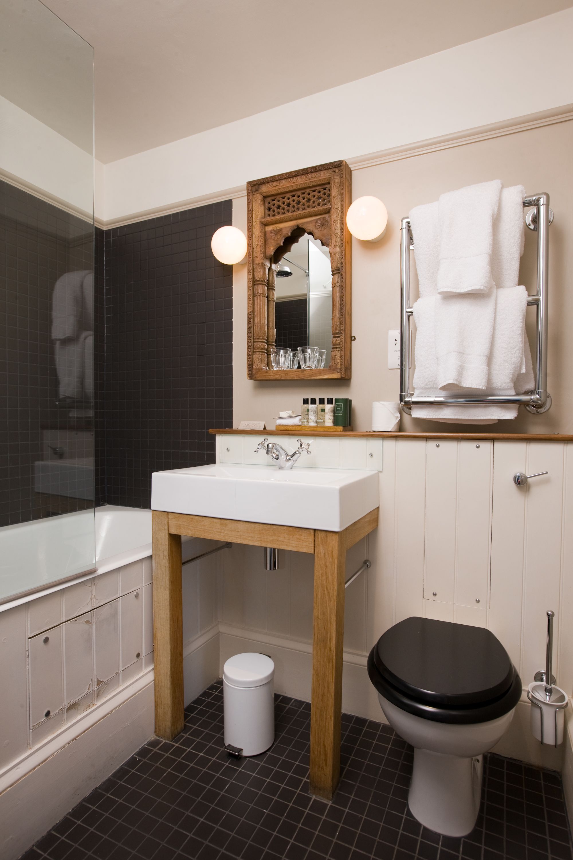A modern bathroom with a white sink, wooden vanity, black toilet, and a large mirror with lights.