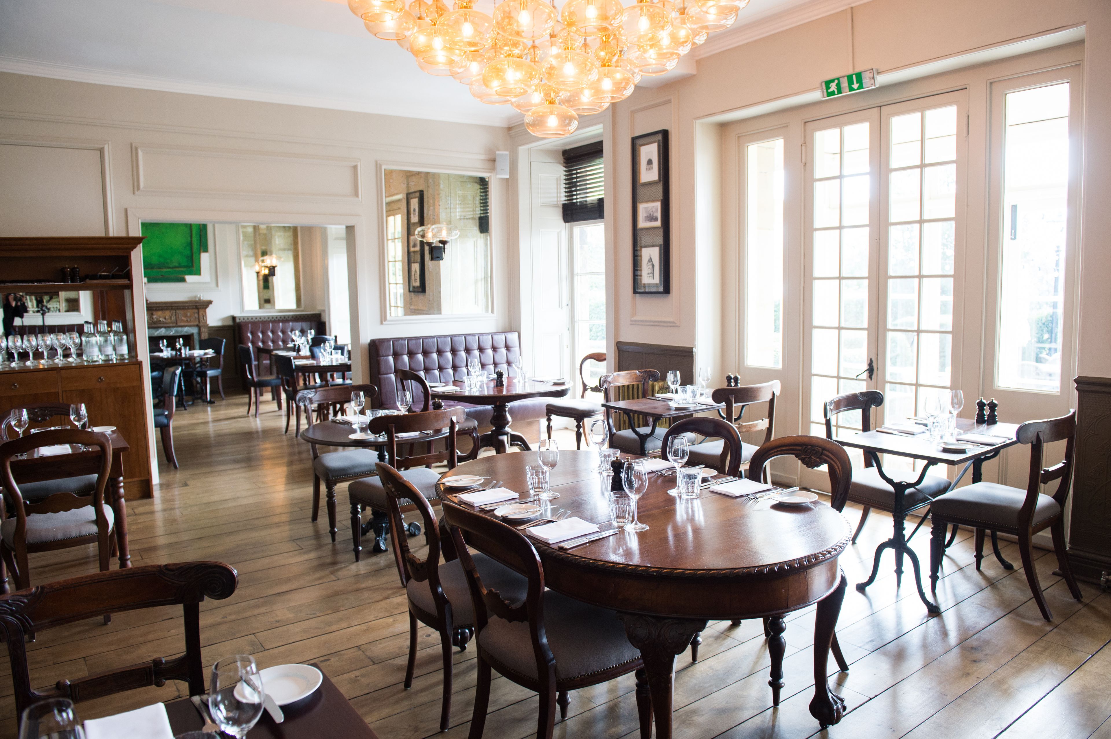 A dining area with wooden tables and chairs, a chandelier, and large windows.