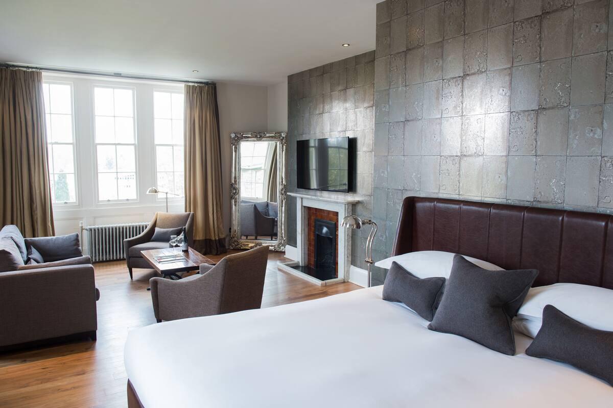 A hotel room with a large bed, a television mounted on the wall, a fireplace, and a seating area with a table and chairs.