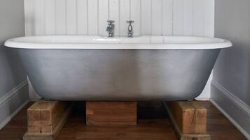 A clawfoot bathtub with a white interior, mounted on wooden supports, in a room with wooden flooring and white paneled walls.
