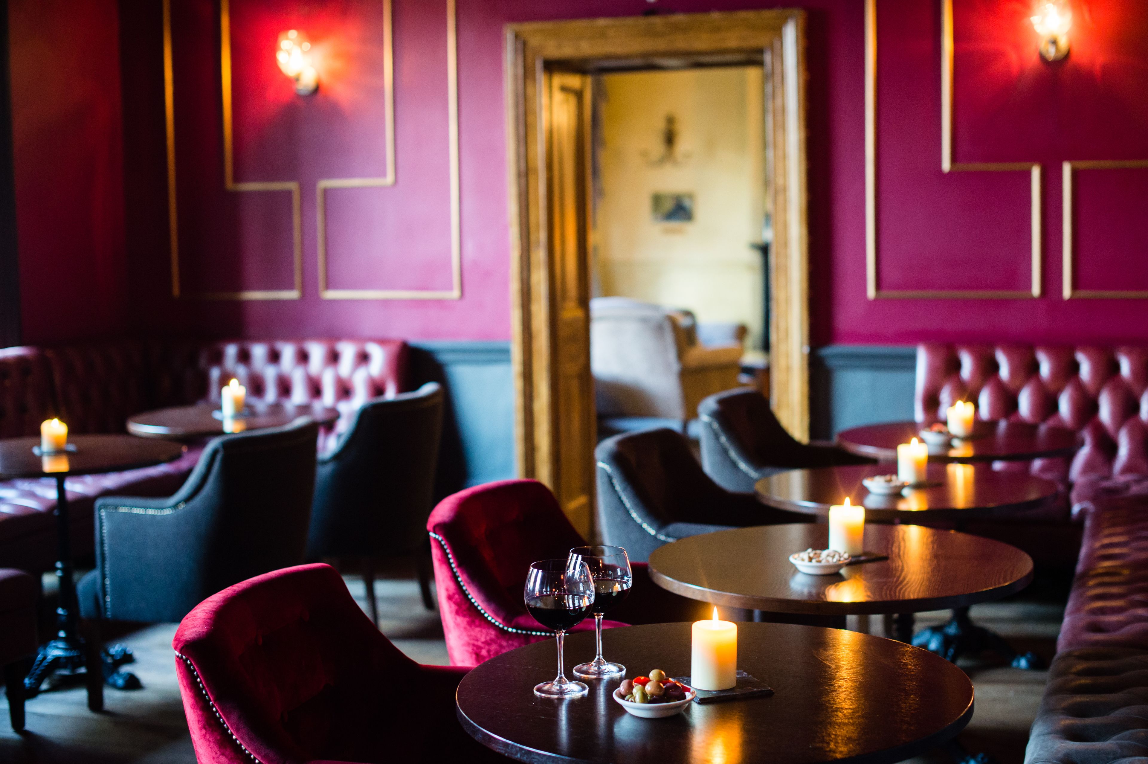 Un restaurant à la lumière tamisée, avec des fauteuils en velours rouge, des tables rondes et des bougies.