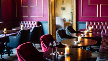 Un restaurant à la lumière tamisée, avec des fauteuils en velours rouge, des tables rondes et des bougies.