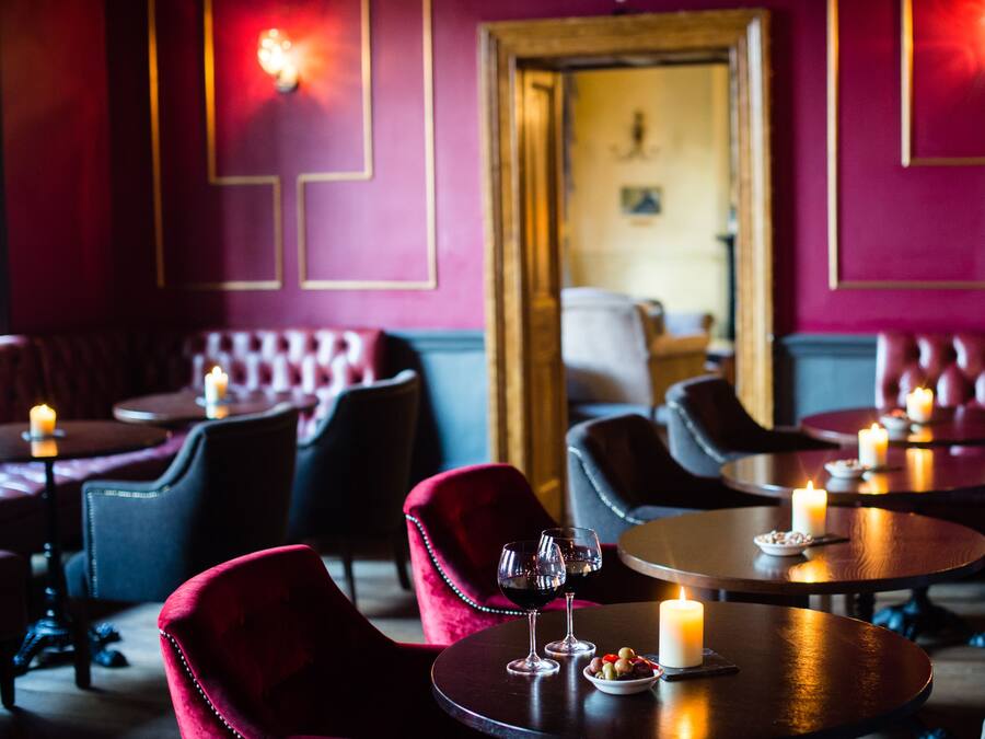 Un restaurant à la lumière tamisée, avec des fauteuils en velours rouge, des tables rondes et des bougies.