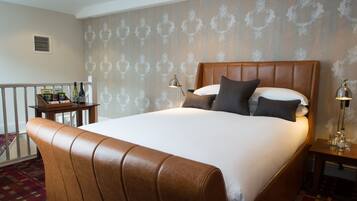 Een hotelkamer met een groot bed, een houten hoofdeinde, een nachtkastje met een lamp en een klein tafeltje met een mand met spullen.