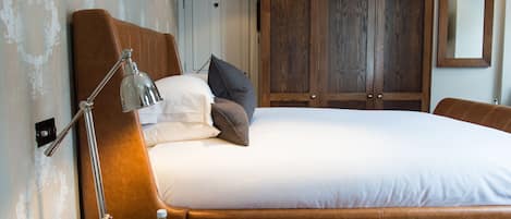 A neatly made bed with pillows, a bedside lamp, and a nightstand with glasses and a bottle.