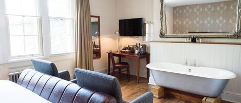 A room with a large window, a bathtub, a desk with a chair, and a television.