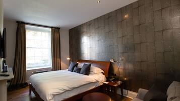 A bedroom with a large bed, a bedside table with a lamp, a small round table, and a sofa.