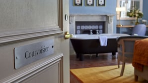Una habitación con una puerta que dice "Courvoisier", una bañera negra, una chimenea y cuadros enmarcados en la pared.