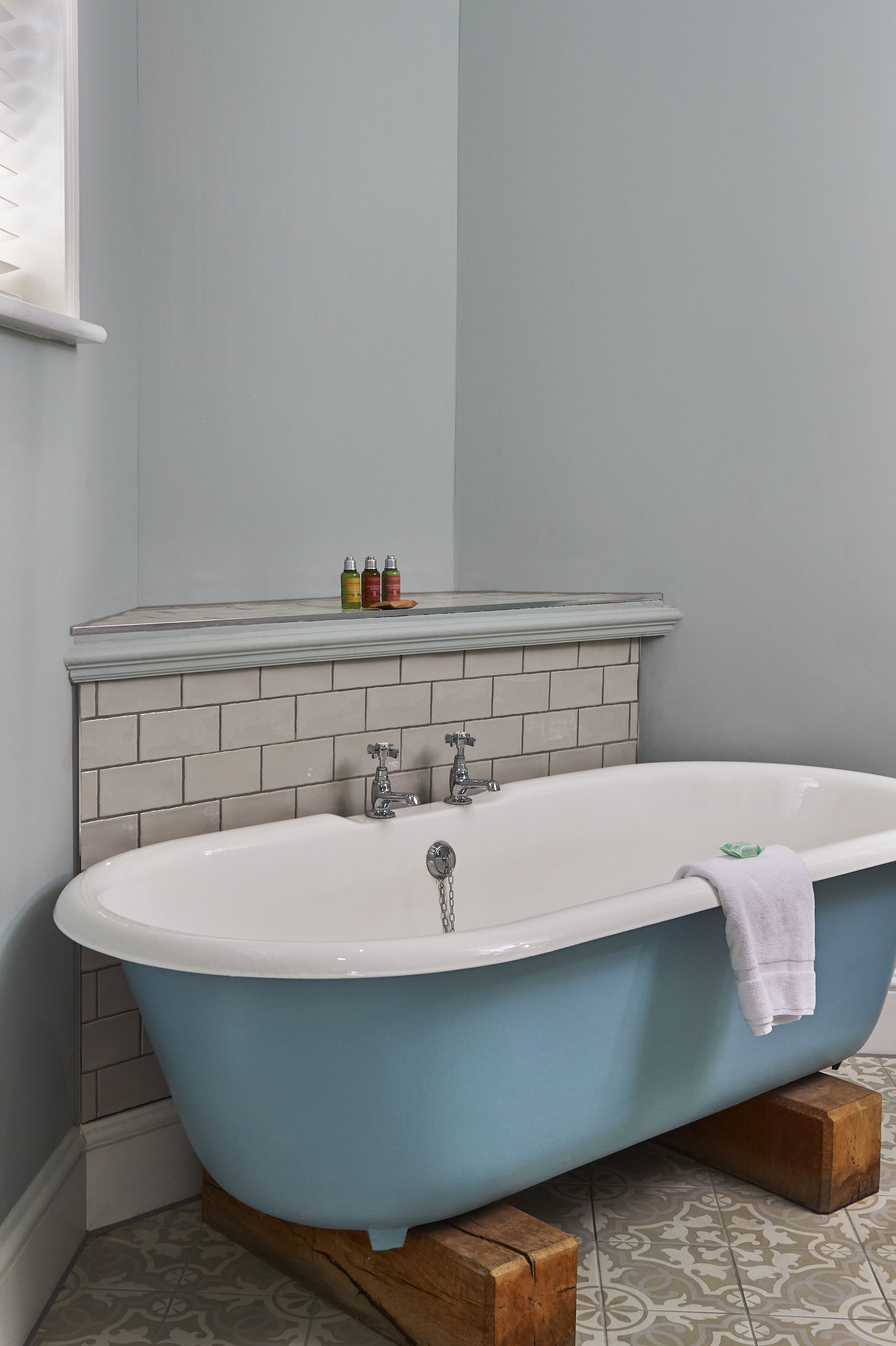 Une salle de bain avec une baignoire sur pieds, un mur carrelé et une étagère contenant des articles de toilette.