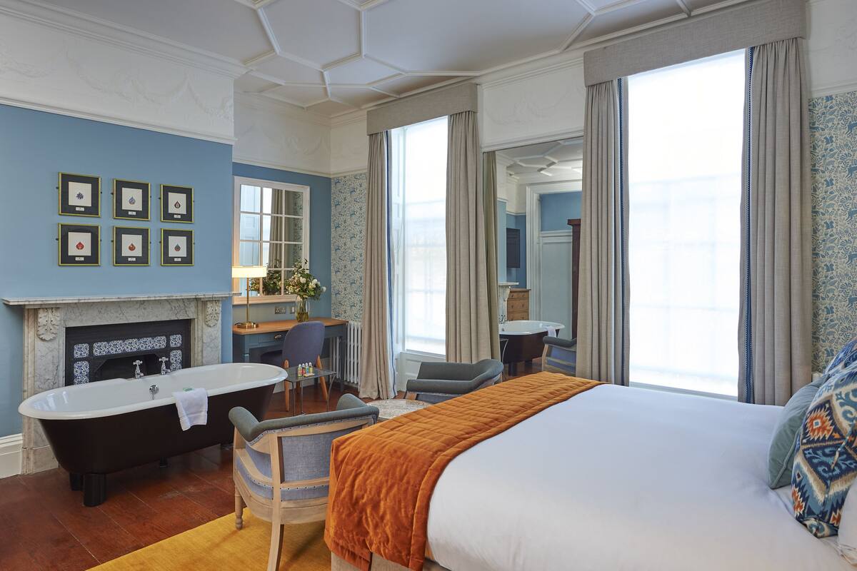 Habitación de hotel con una cama grande, una bañera, un escritorio y vista al mar.