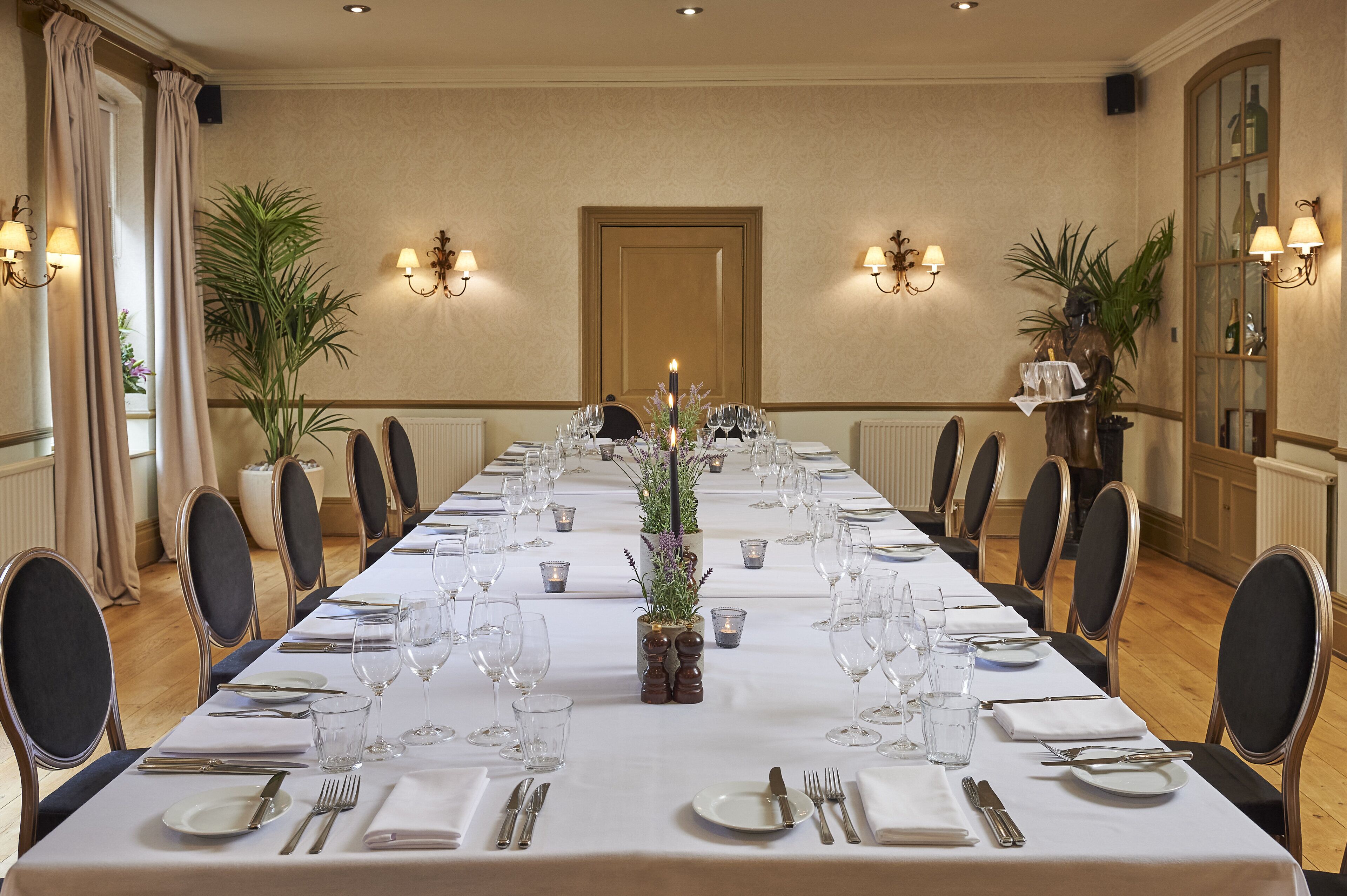 Una larga mesa de comedor preparada para un evento formal, con sillas, velas y vajilla.