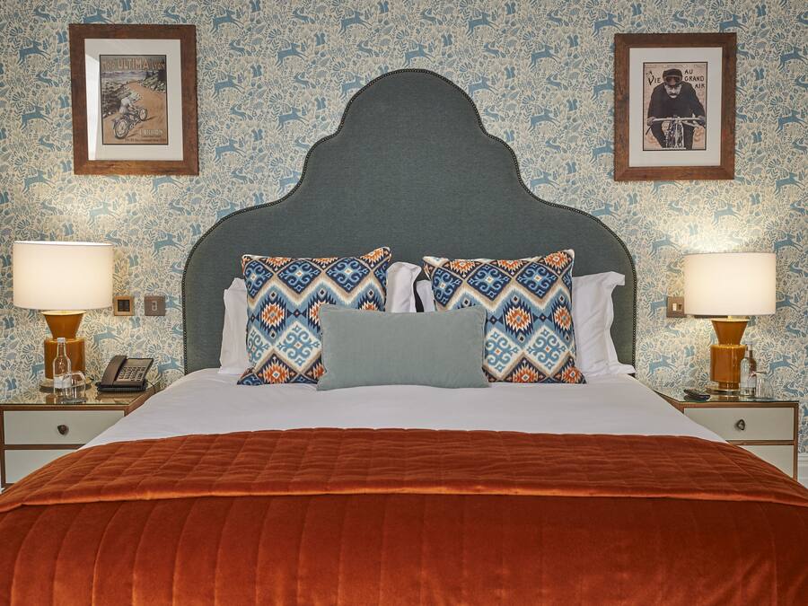 A neatly made bed with patterned pillows, a dark headboard, and two bedside tables with lamps and a phone.