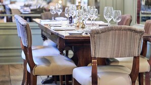 Una larga mesa de comedor con numerosas sillas, elegante vajilla y velas, en una habitación amplia y bien iluminada con techos altos y molduras decorativas.