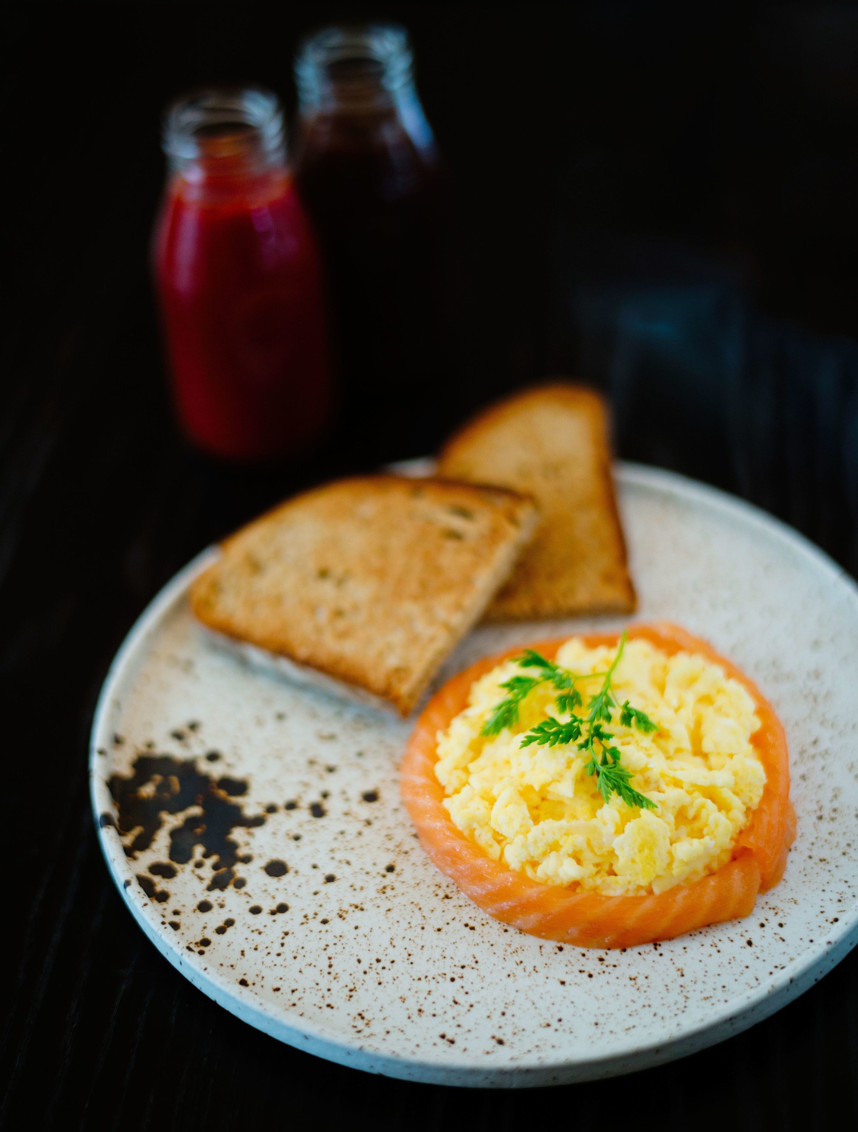 Une assiette contenant des œufs brouillés et une tranche de saumon, accompagnée de deux tranches de pain grillé, le tout présenté sur une assiette en céramique à motifs.